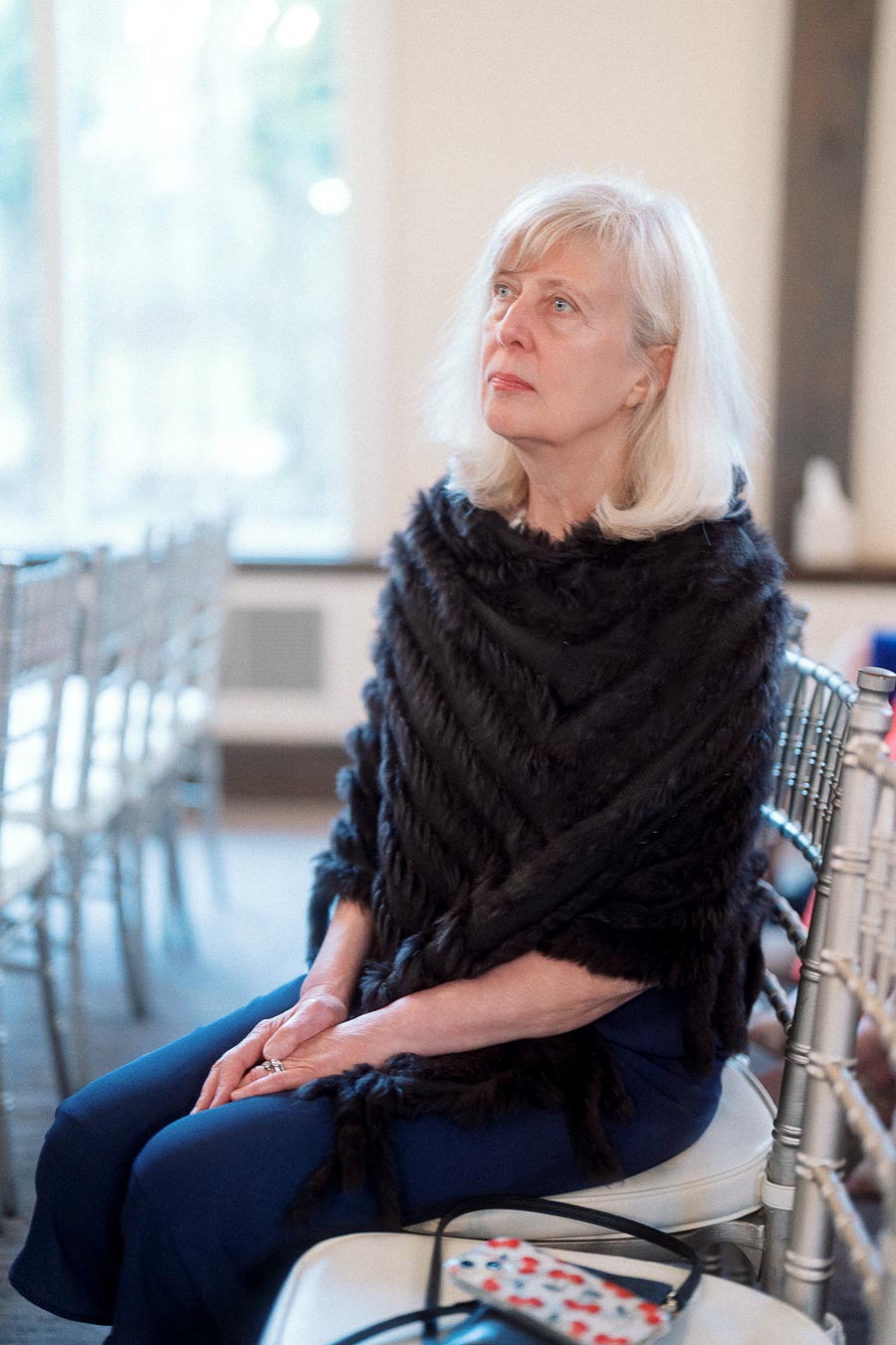 Older woman seated on a silver chair indoors, looking upward thoughtfully.