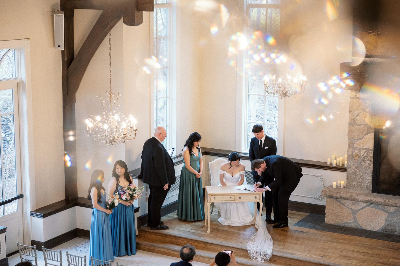 Couple signing documents during an indoor wedding ceremony with attendants nearby.