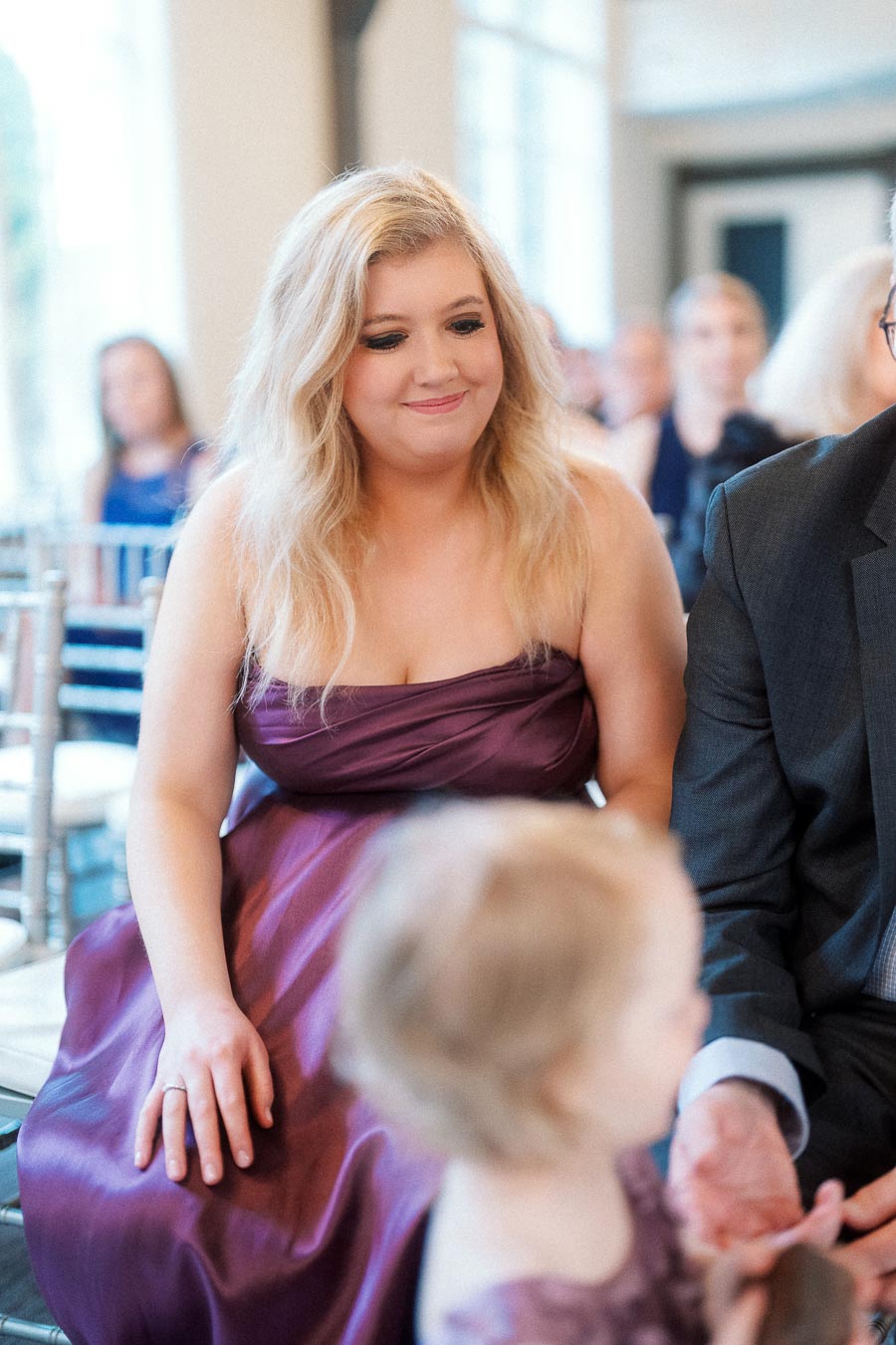 Woman in a purple formal dress seated indoors beside other guests