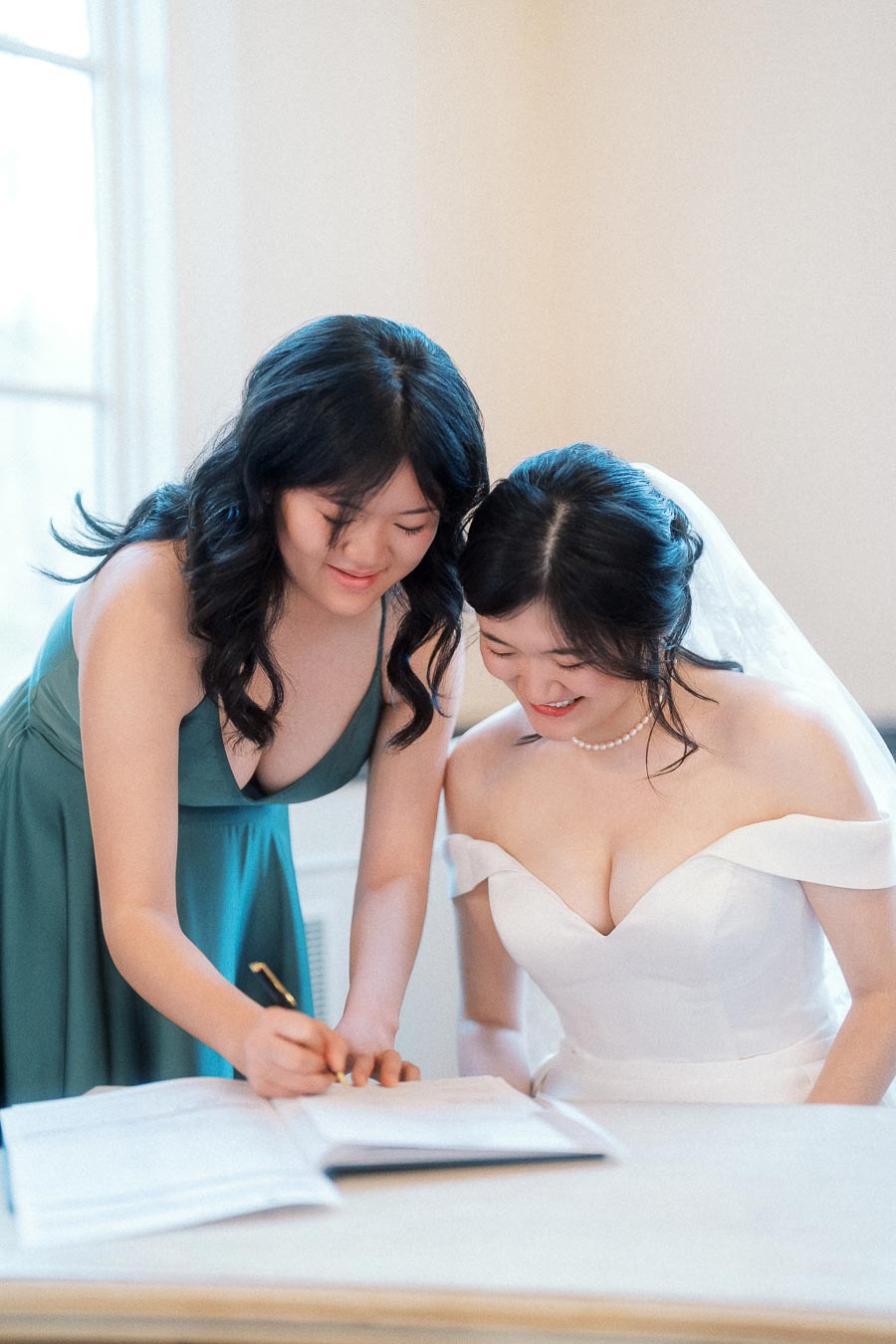 Bride and attendant signing a document indoors during a wedding moment
