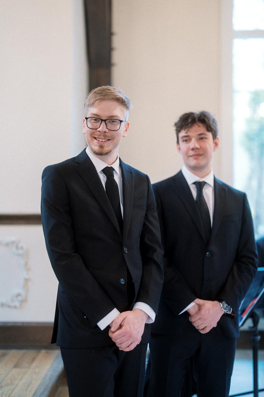 Two men in black suits standing indoors during an engagement photoshoot