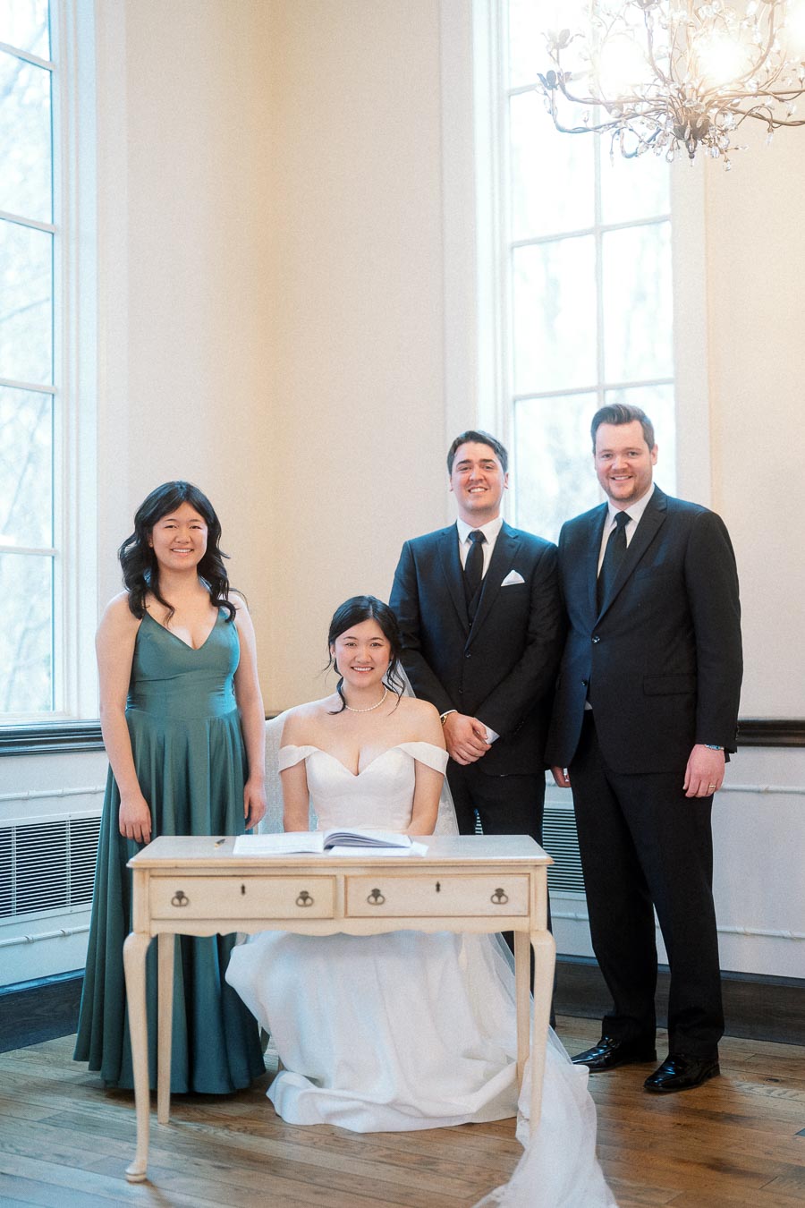Formal group portrait with a seated woman in a white gown beside three attendants indoors