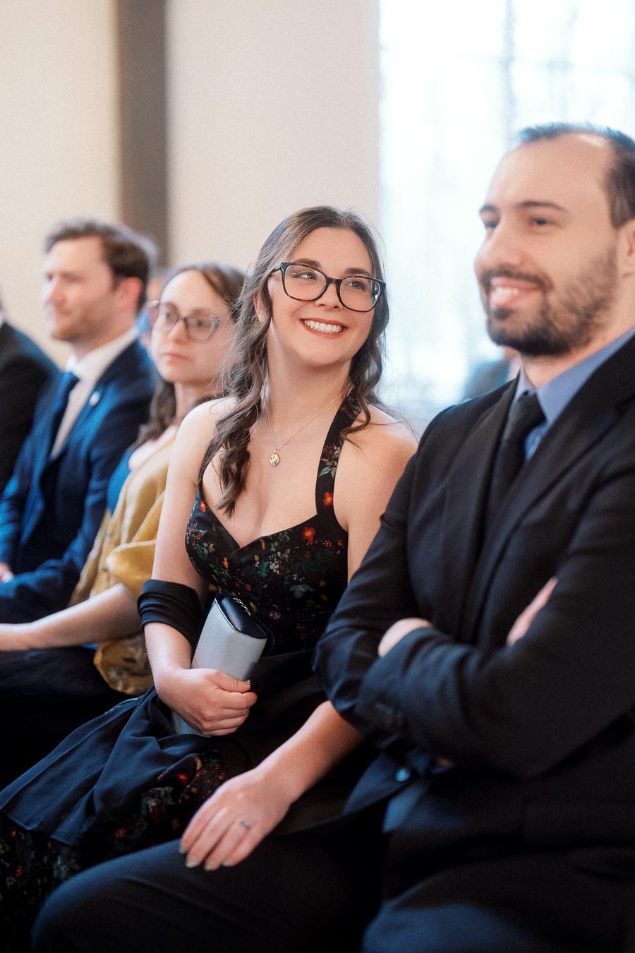 Couple seated indoors during an engagement photoshoot, smiling among other guests.