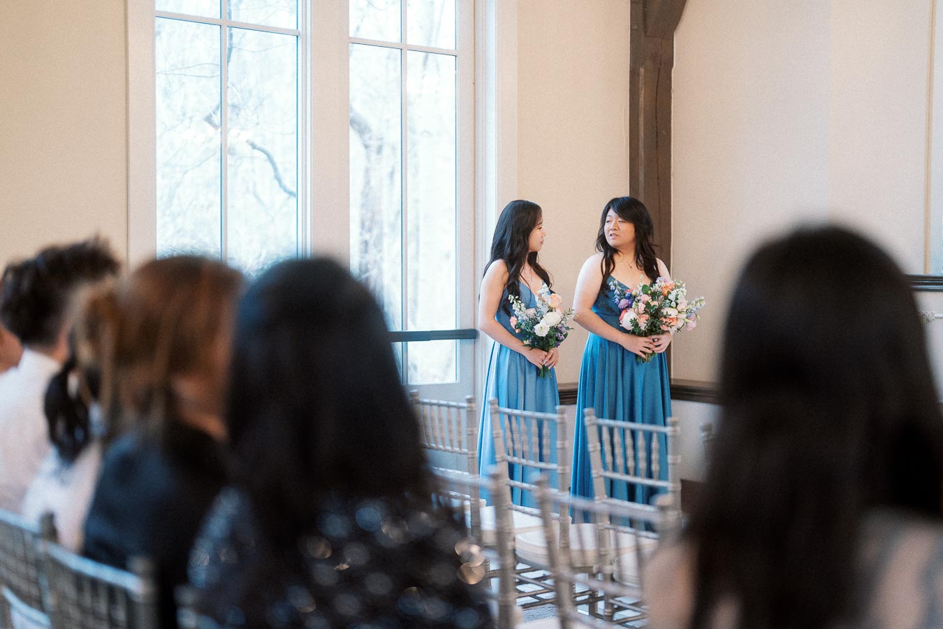 Two bridesmaids in blue dresses holding bouquets during an indoor ceremony