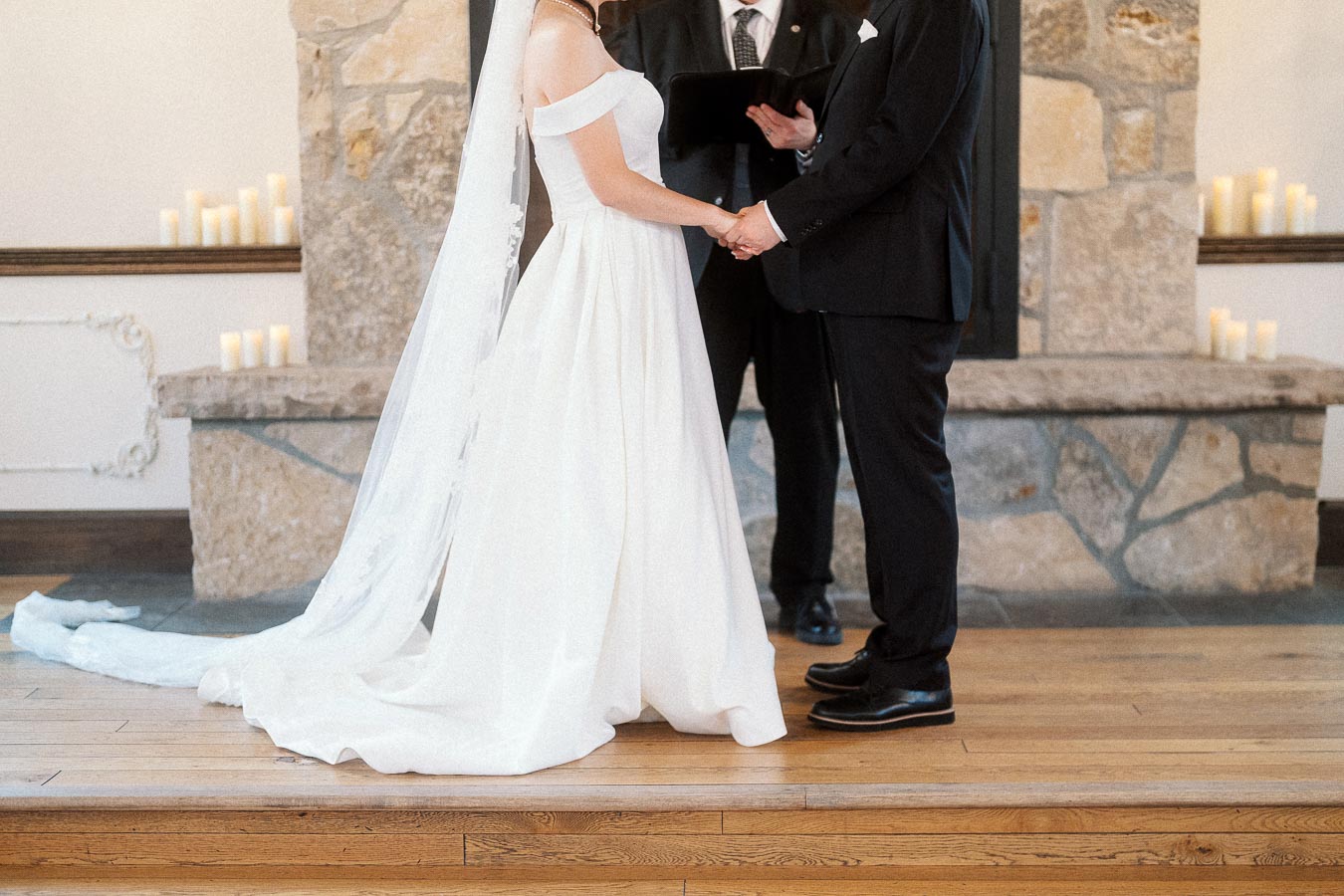 Couple holding hands during an indoor wedding ceremony by a stone fireplace