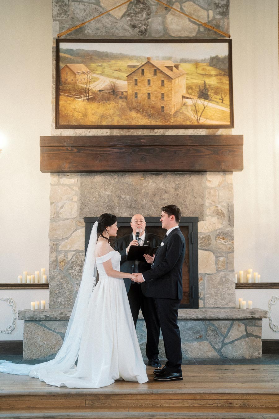 Couple holding hands during an indoor wedding ceremony in front of a stone fireplace