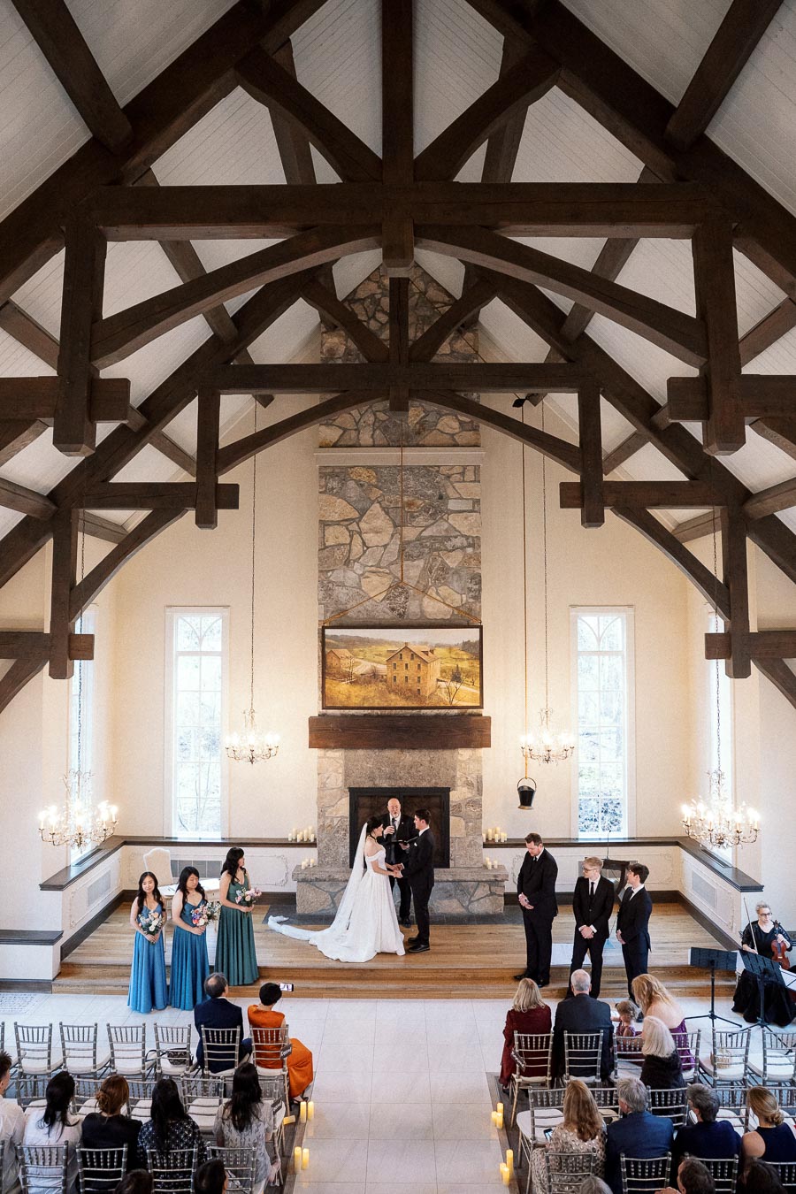 Wedding ceremony inside a chapel with timber beams, stone fireplace, and seated guests.