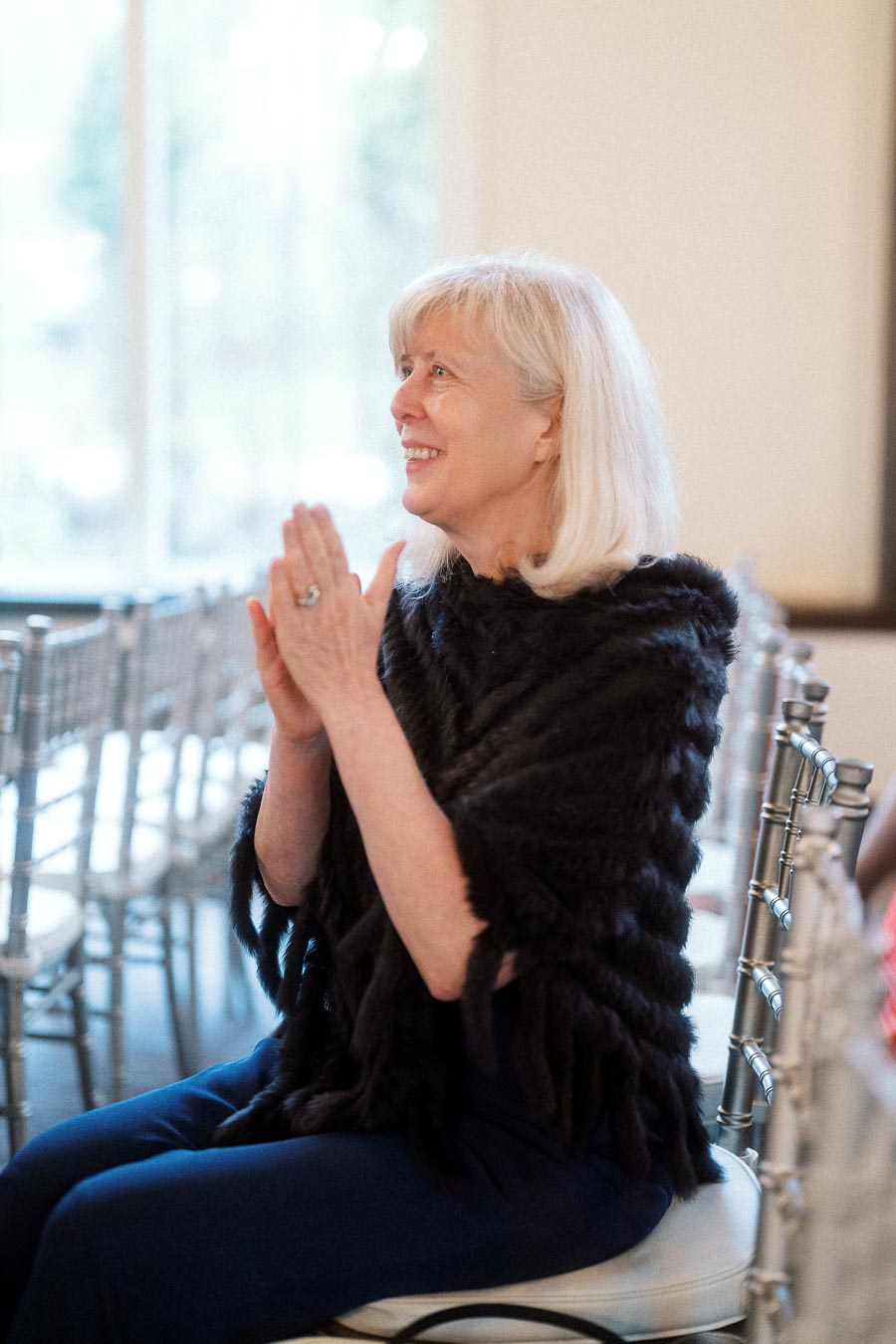 Woman seated indoors, smiling with hands clasped during an engagement event