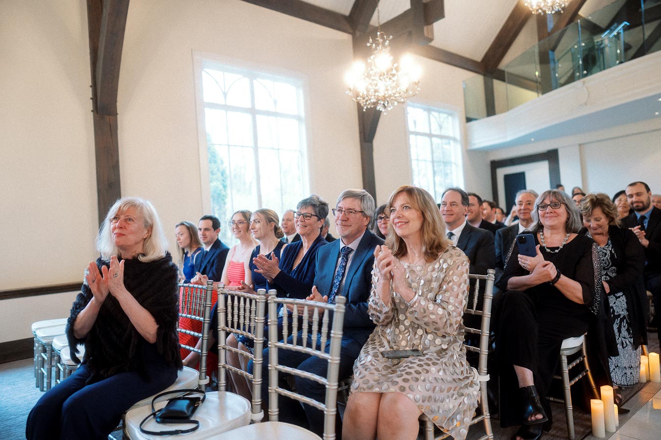 Seated guests applauding during an indoor ceremony in a bright hall