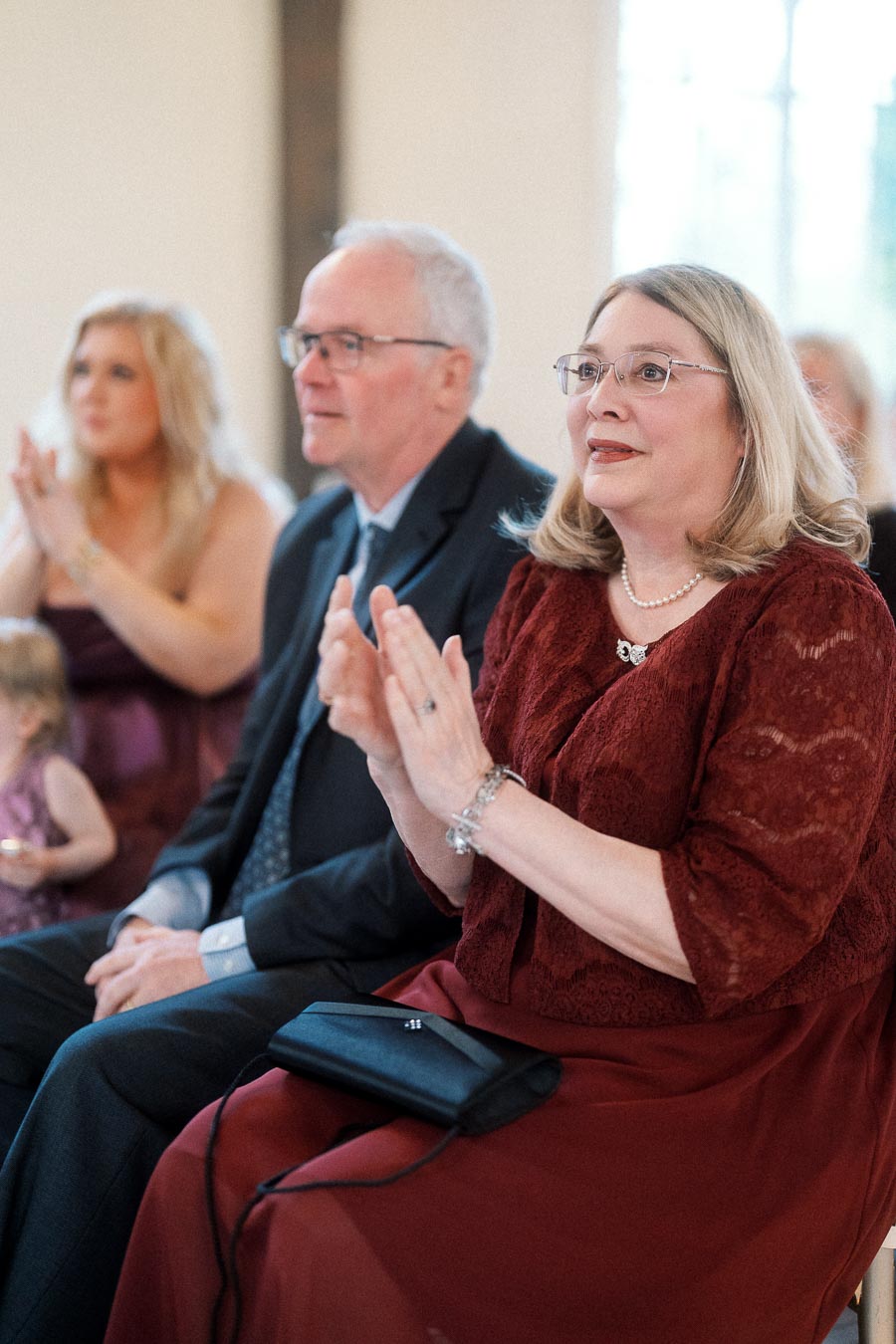 Seated guests in formal attire applauding during an indoor celebration.