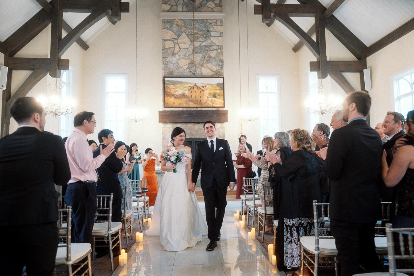 Newlywed couple walking down the aisle as guests applaud inside a chapel.