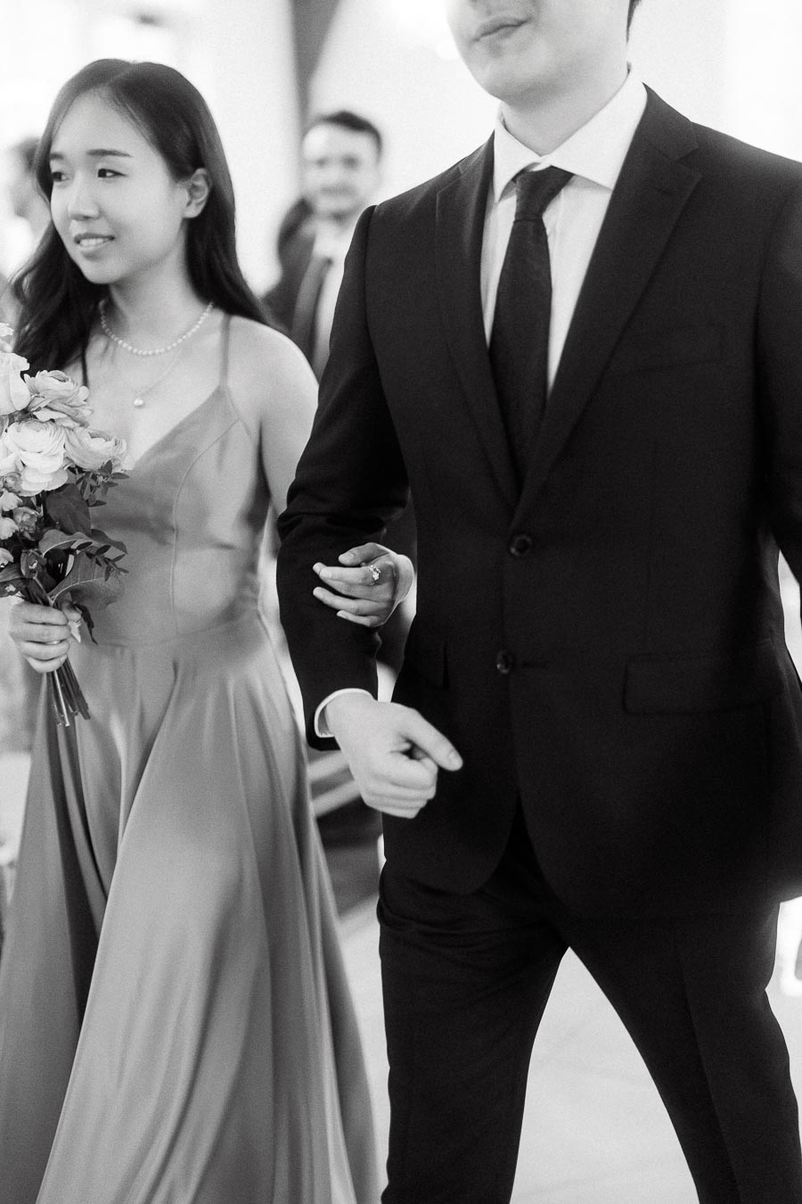 Couple walking arm in arm, with one holding a bouquet during an engagement photoshoot.