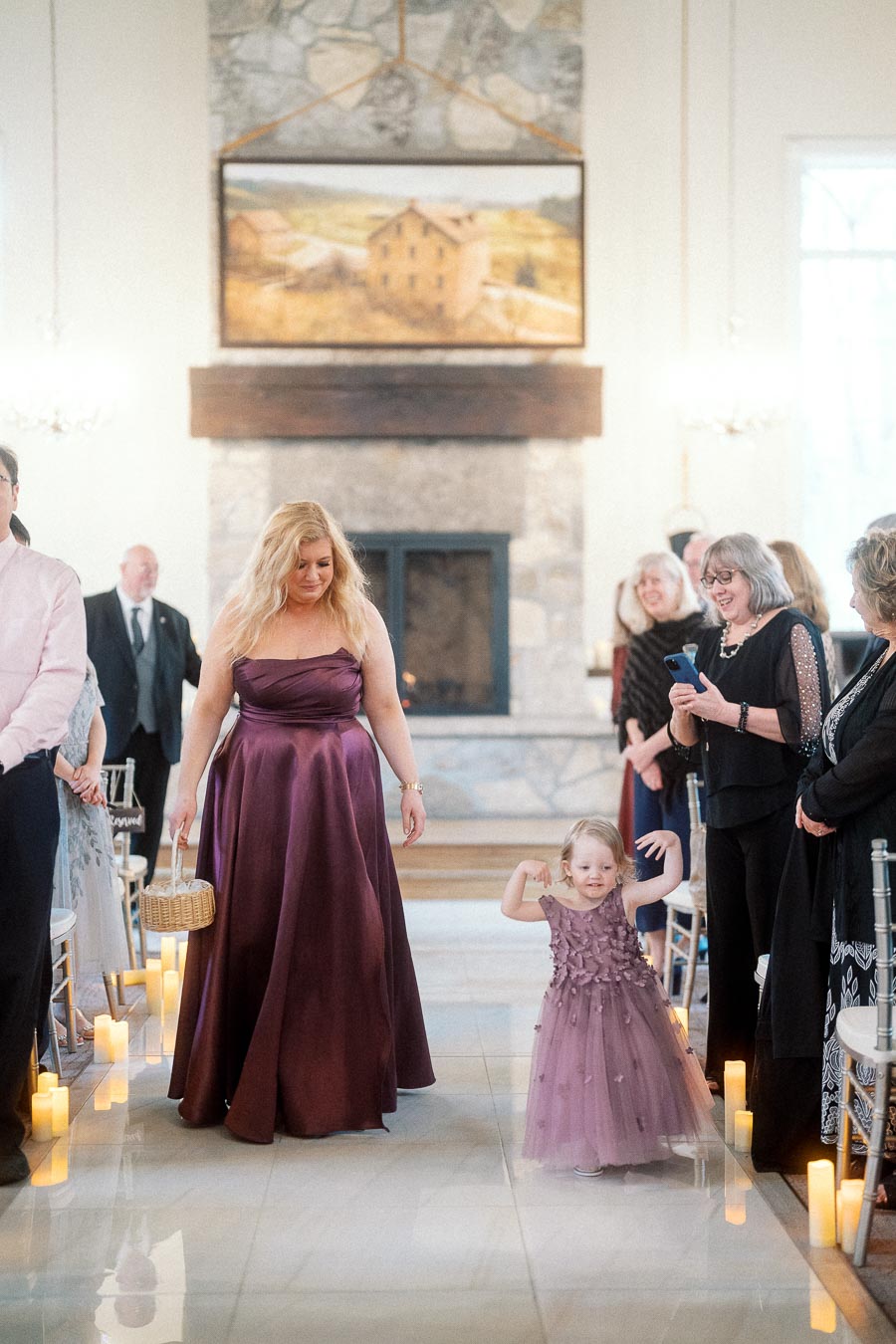 Young flower girl walking down a candlelit wedding aisle with a bridesmaid
