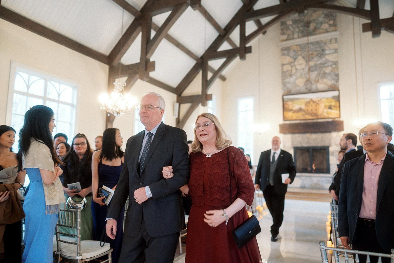Well-dressed couple walking arm in arm down an aisle inside a bright timber-framed hall