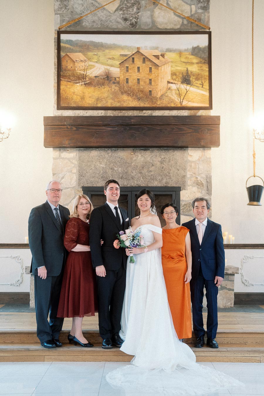 Wedding couple posing with family in front of a stone fireplace indoors