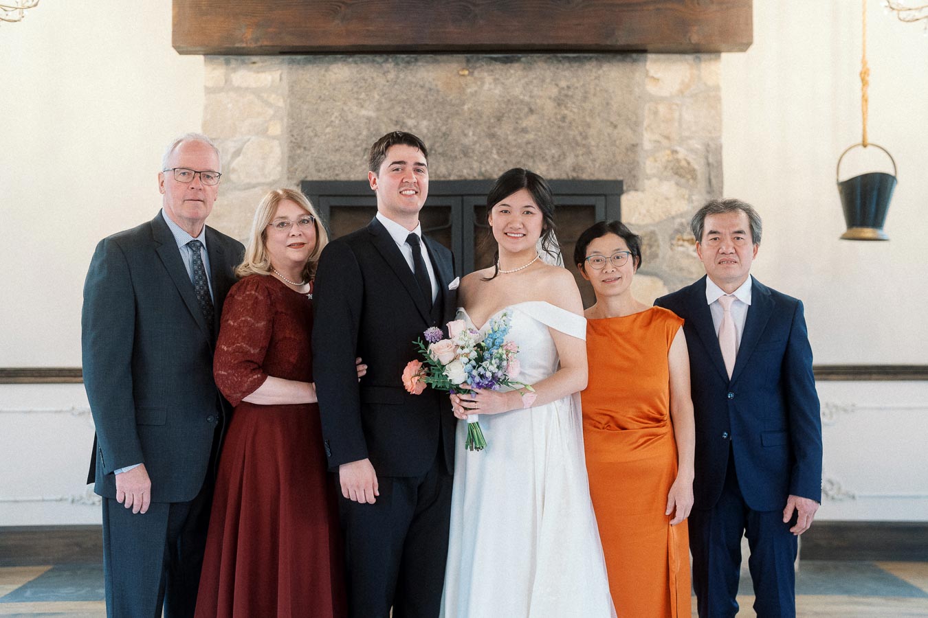 Bride and groom posing with family indoors in front of a stone fireplace