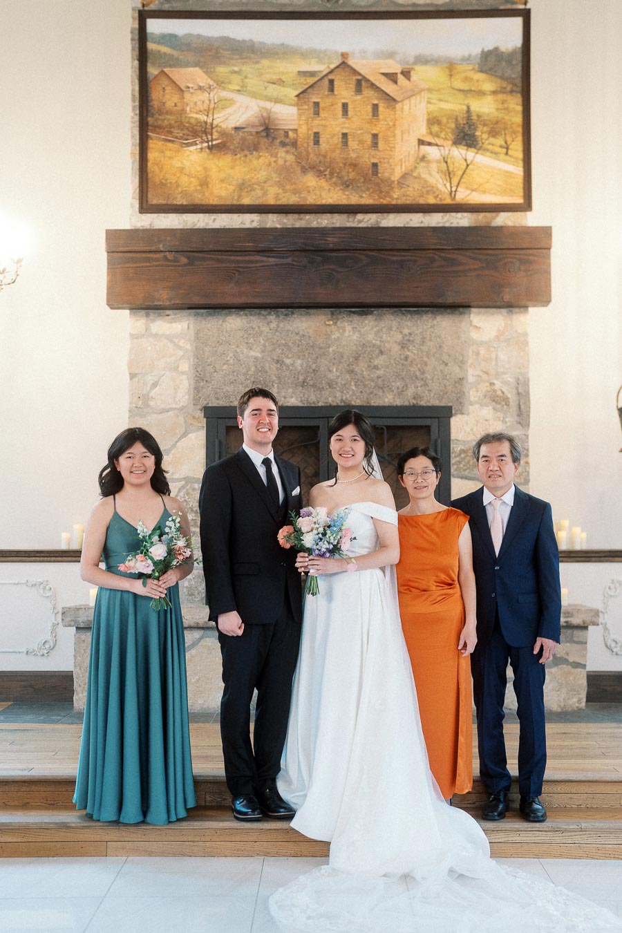 Wedding couple posing with three family members in front of a stone fireplace.