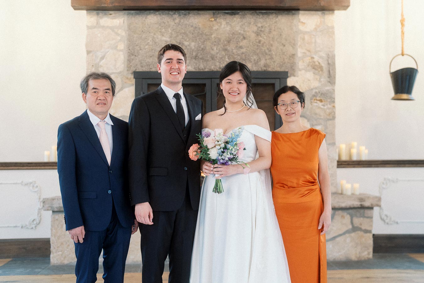 Wedding couple posing with two family members in front of a stone fireplace