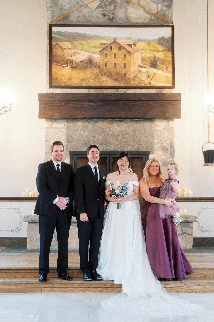 Wedding party portrait in front of a stone fireplace with the bride holding a bouquet