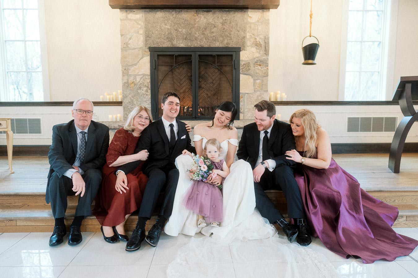Wedding party seated by a stone fireplace with bride, groom, child, and family members.