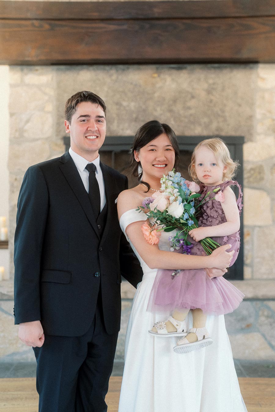 Couple in formal wedding attire posing with a young child holding flowers.