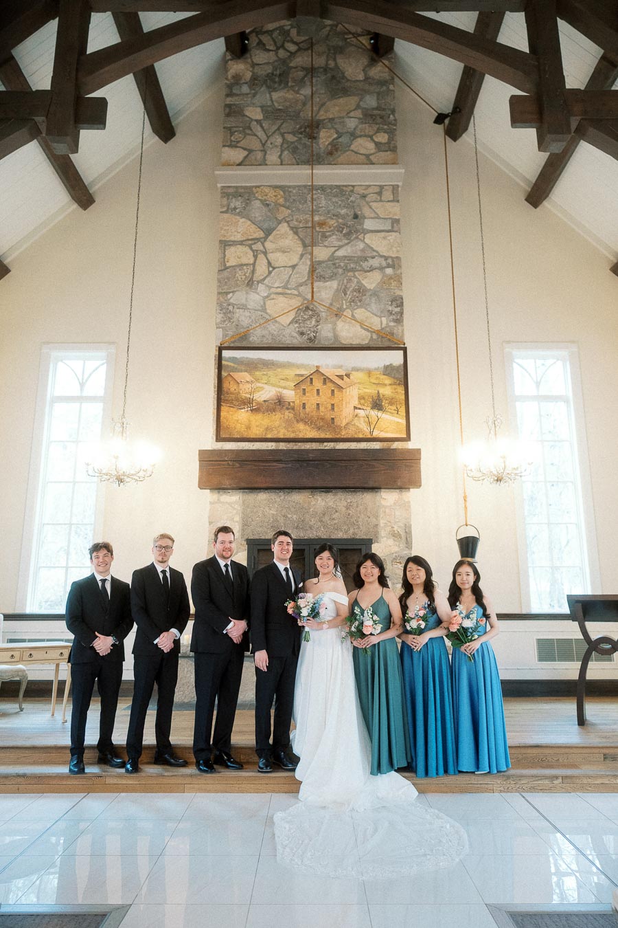 Wedding party standing indoors beneath vaulted beams and a stone fireplace.
