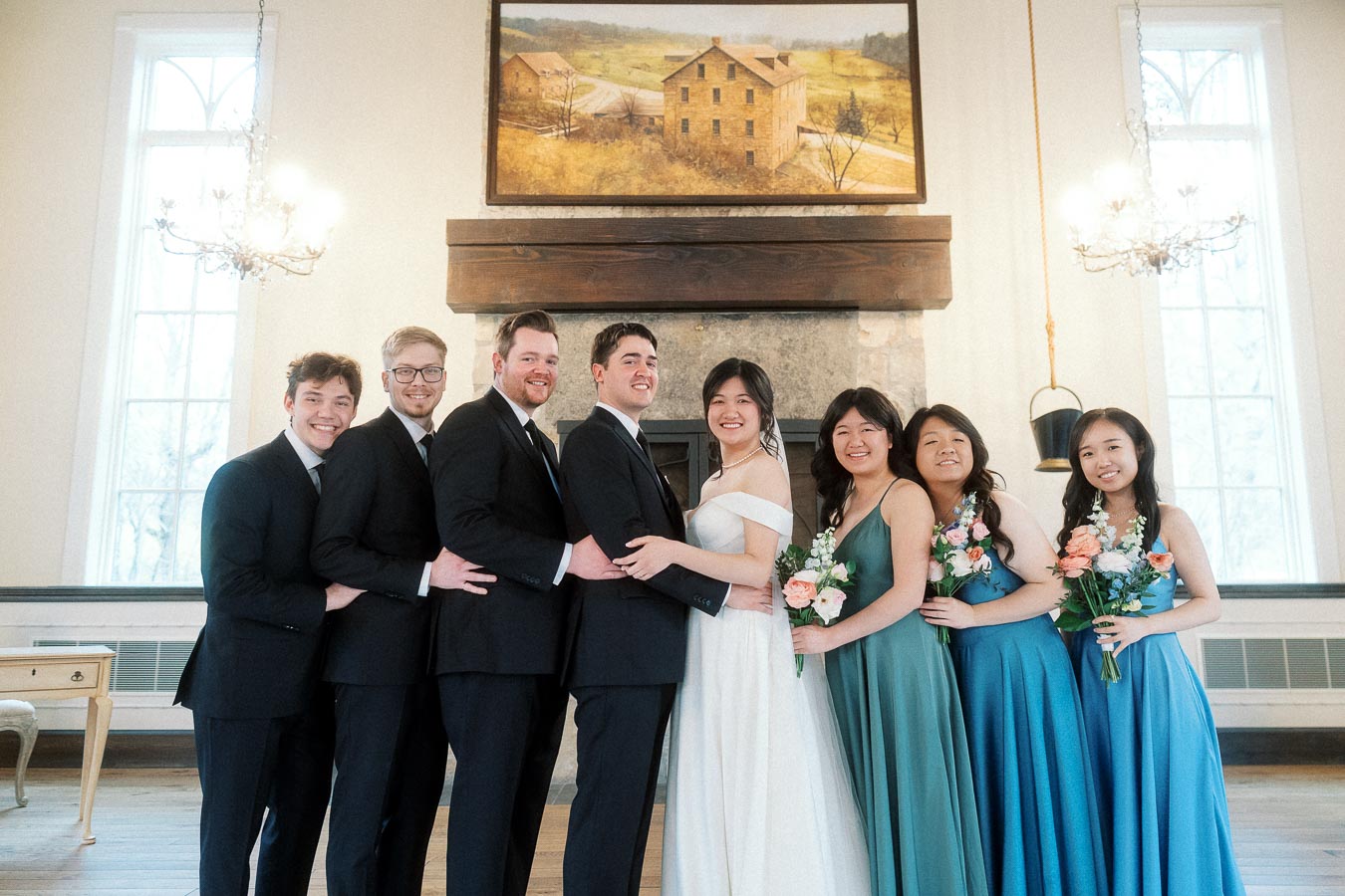 Wedding party posing indoors with bride, groom, bridesmaids, groomsmen, and bouquets.