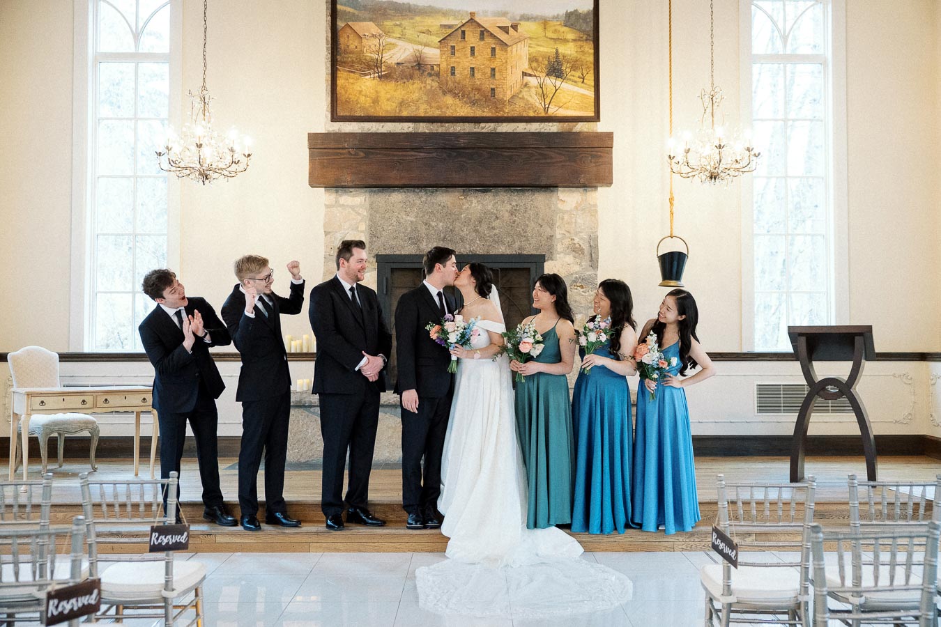 Wedding party watches as bride and groom kiss in an indoor ceremony space