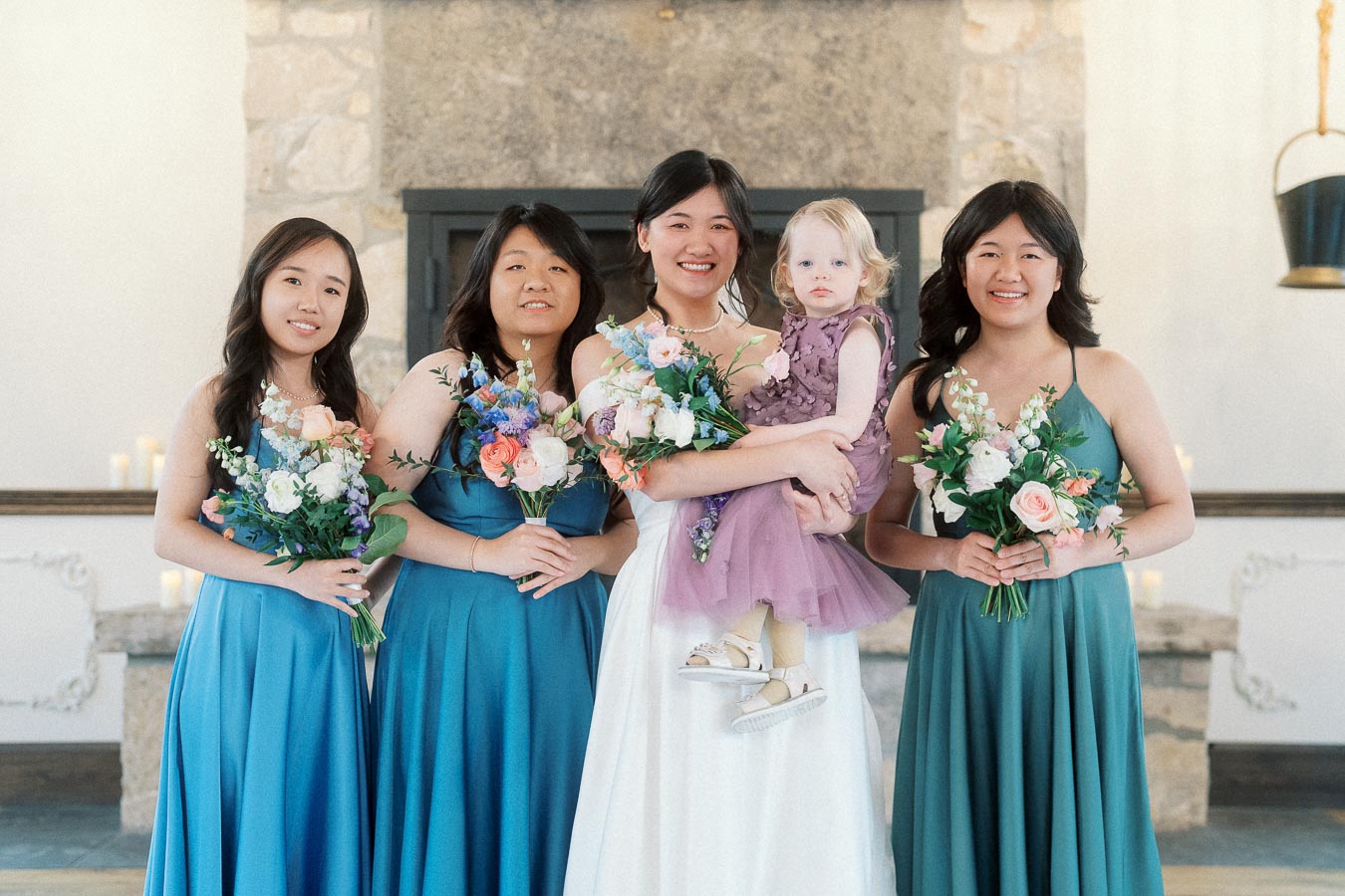 Bride with bridesmaids and a young flower girl holding bouquets indoors