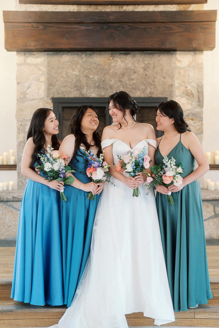 Bride with three bridesmaids holding bouquets in front of a stone fireplace