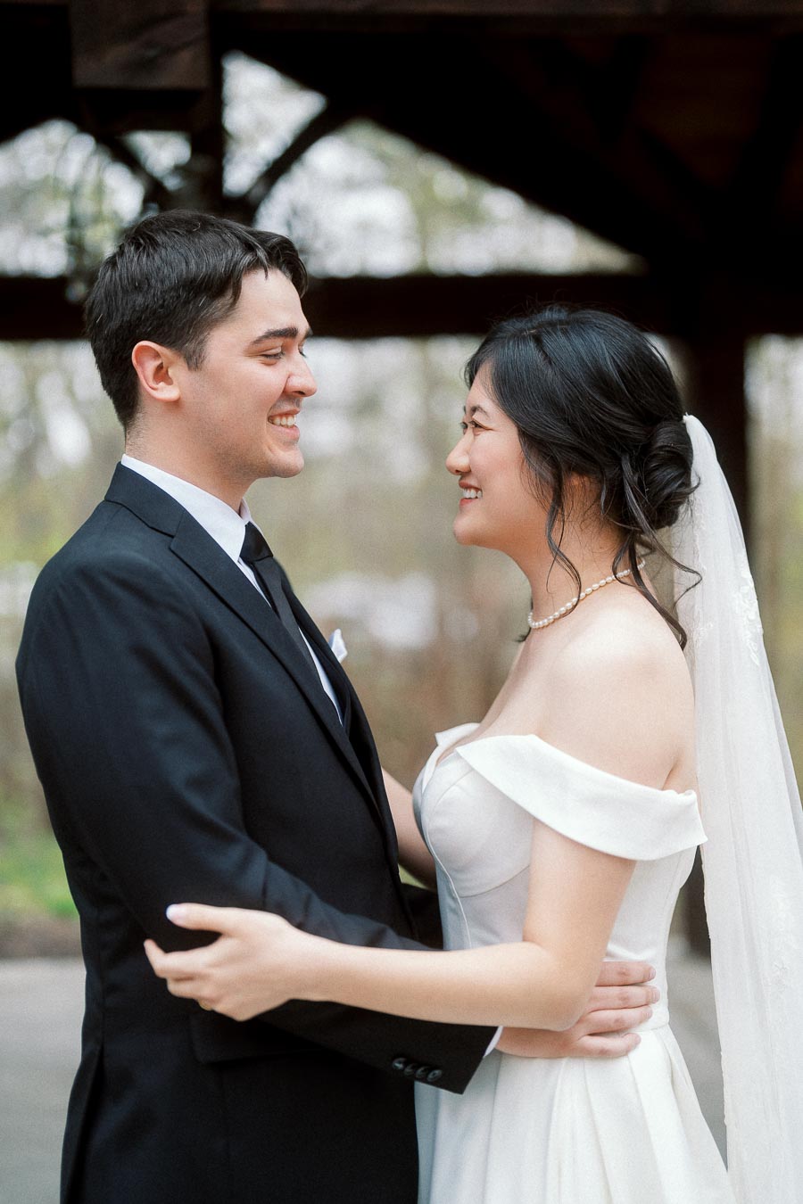 Bride and groom smiling at each other while embracing outdoors