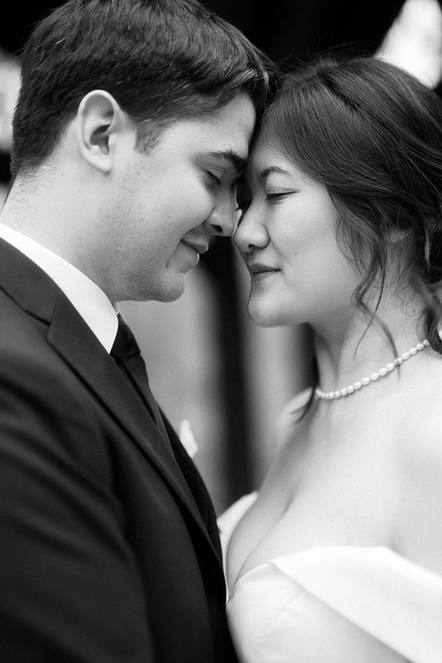 Close-up black-and-white portrait of a couple touching foreheads with eyes closed.