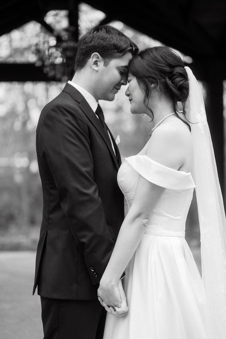 Couple in wedding attire holding hands with their foreheads touching