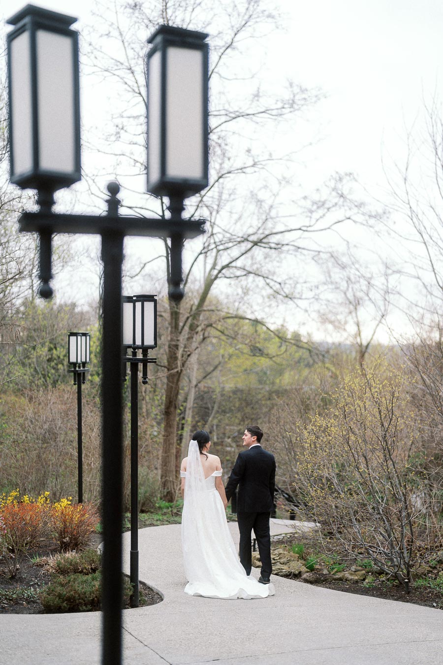 Couple in wedding attire walking hand in hand along a garden path
