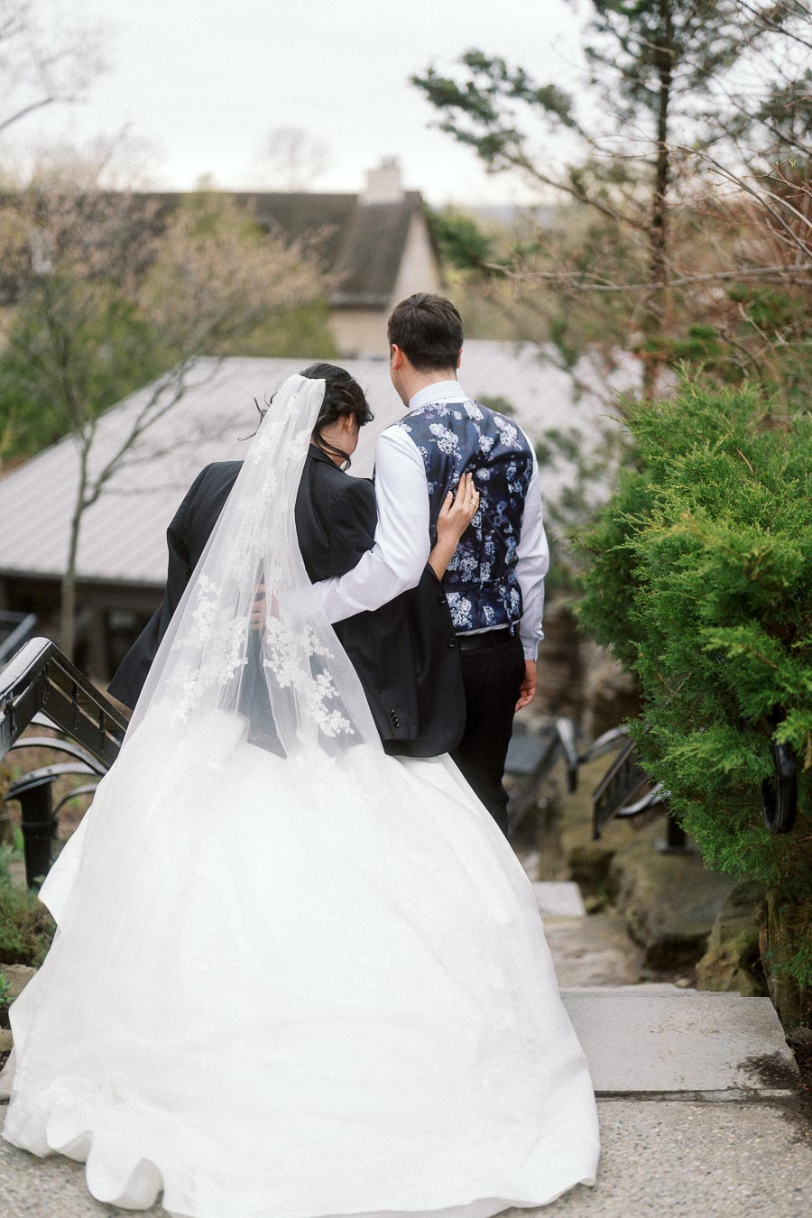 Couple in wedding attire walking down outdoor stone steps together