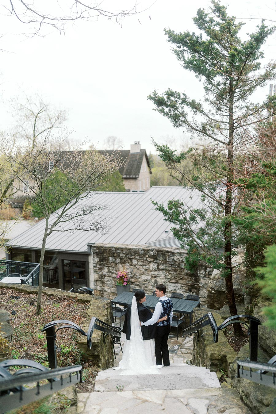Couple in formal wedding attire standing together on stone steps outdoors