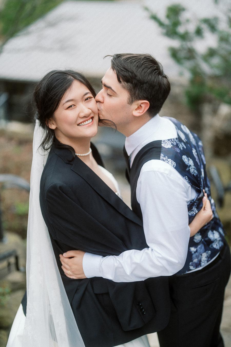 Groom kisses smiling bride on the cheek during an outdoor portrait