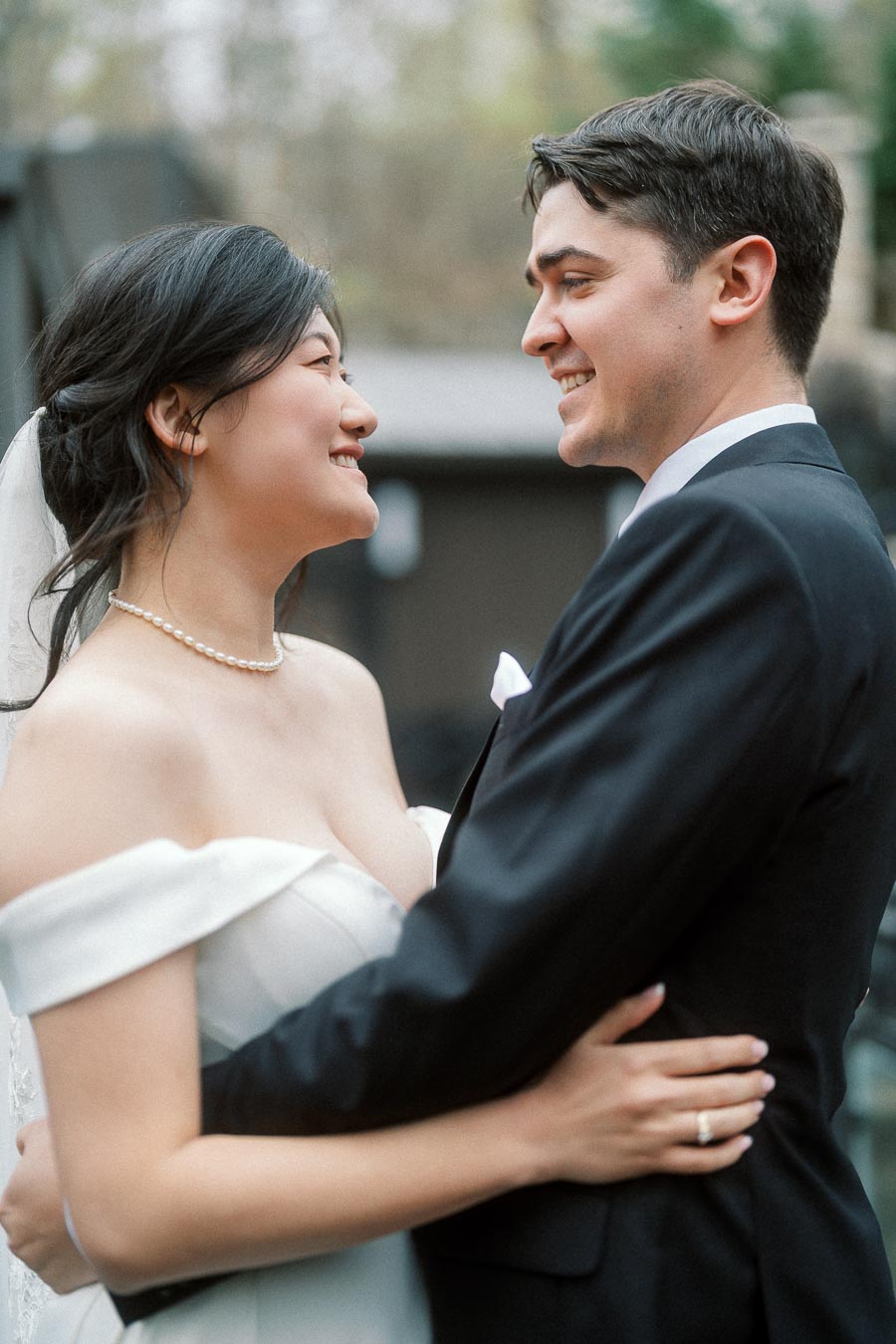 Couple in formal attire smiling at each other while embracing outdoors
