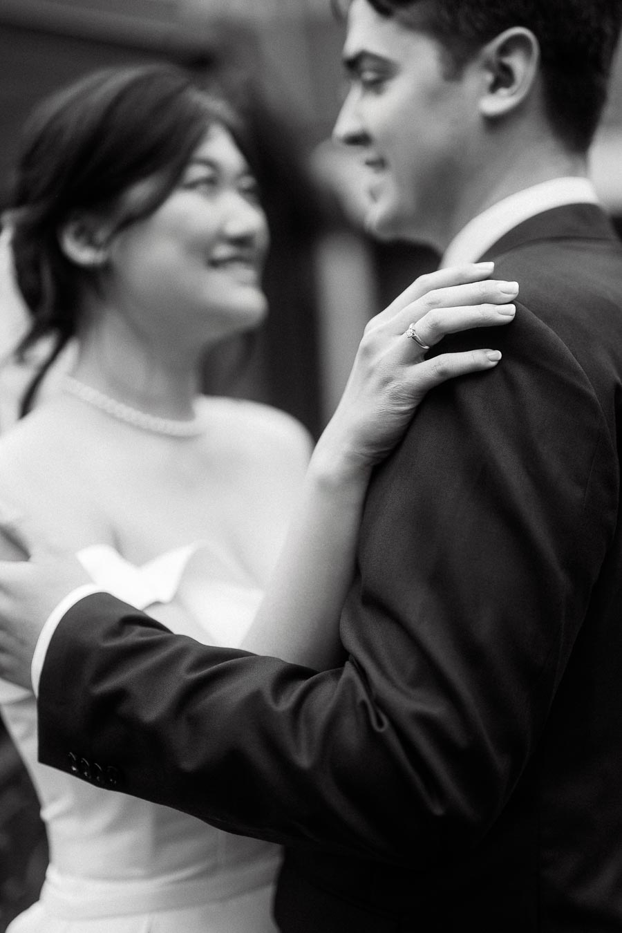Close-up black-and-white portrait of a couple embracing, with an engagement ring visible.