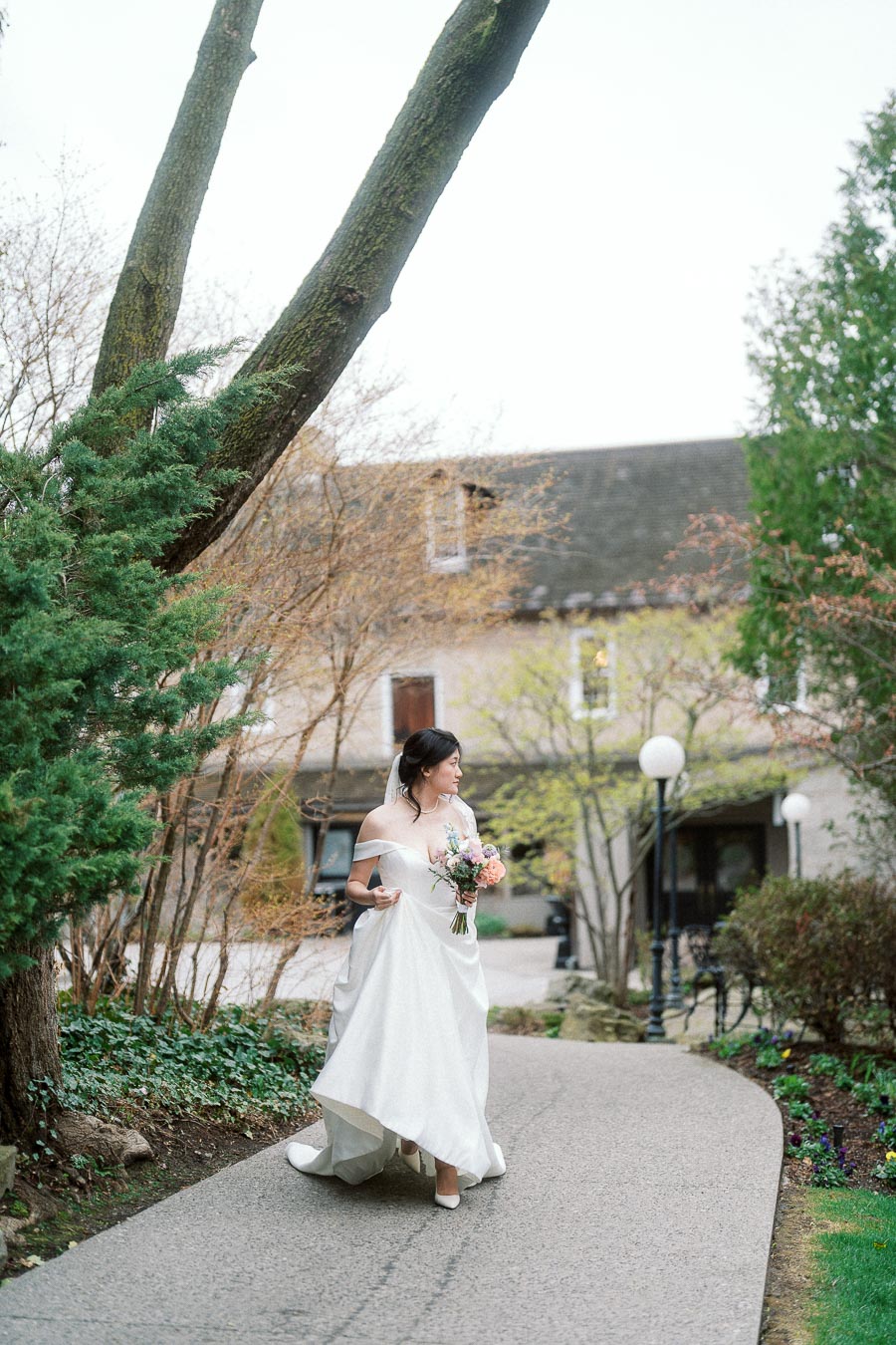 Woman in a white gown holding a bouquet on a garden pathway.