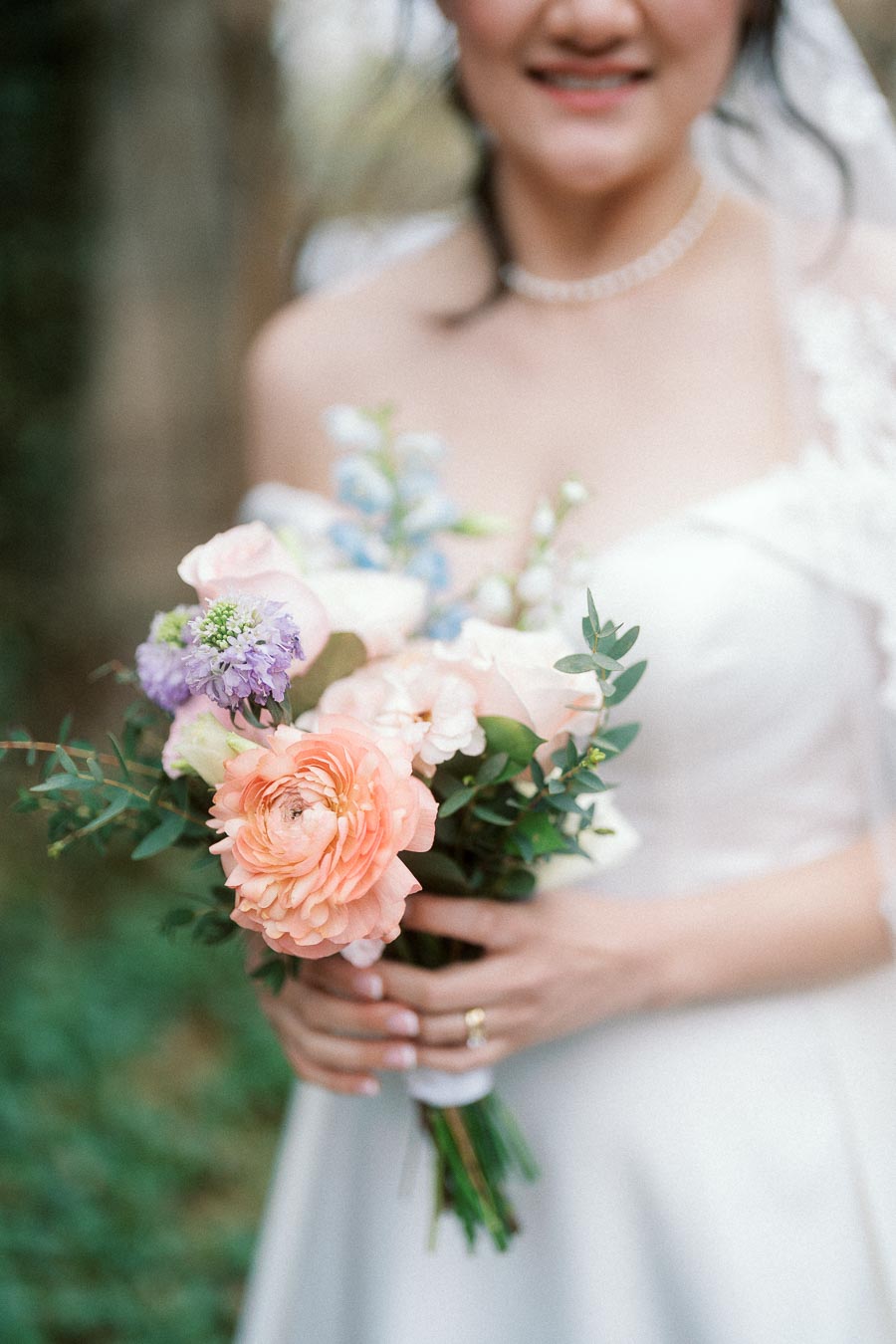 Bride holding a pastel bouquet with peach and lavender flowers outdoors