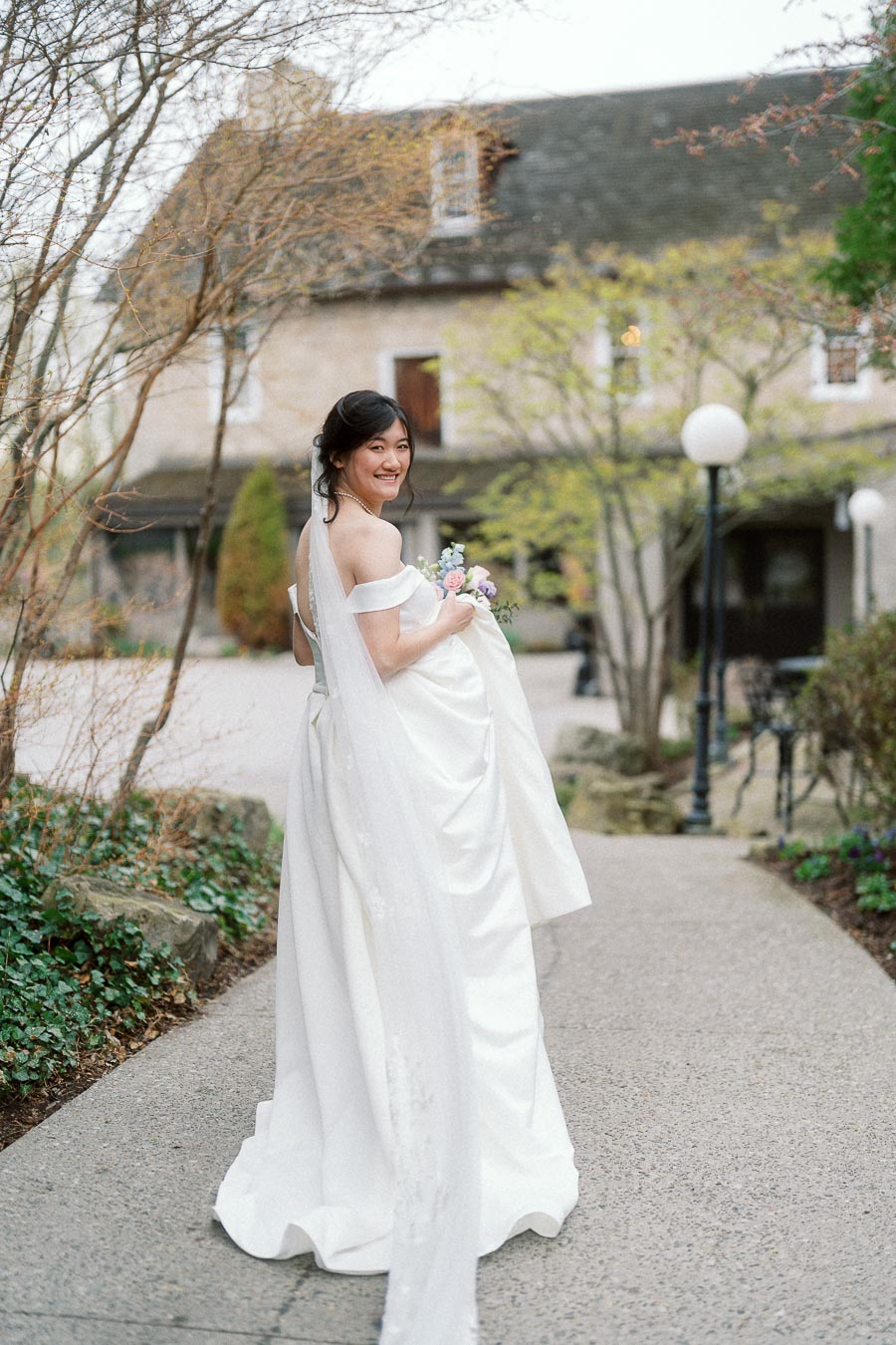 Bride in a white gown looking back on a garden walkway