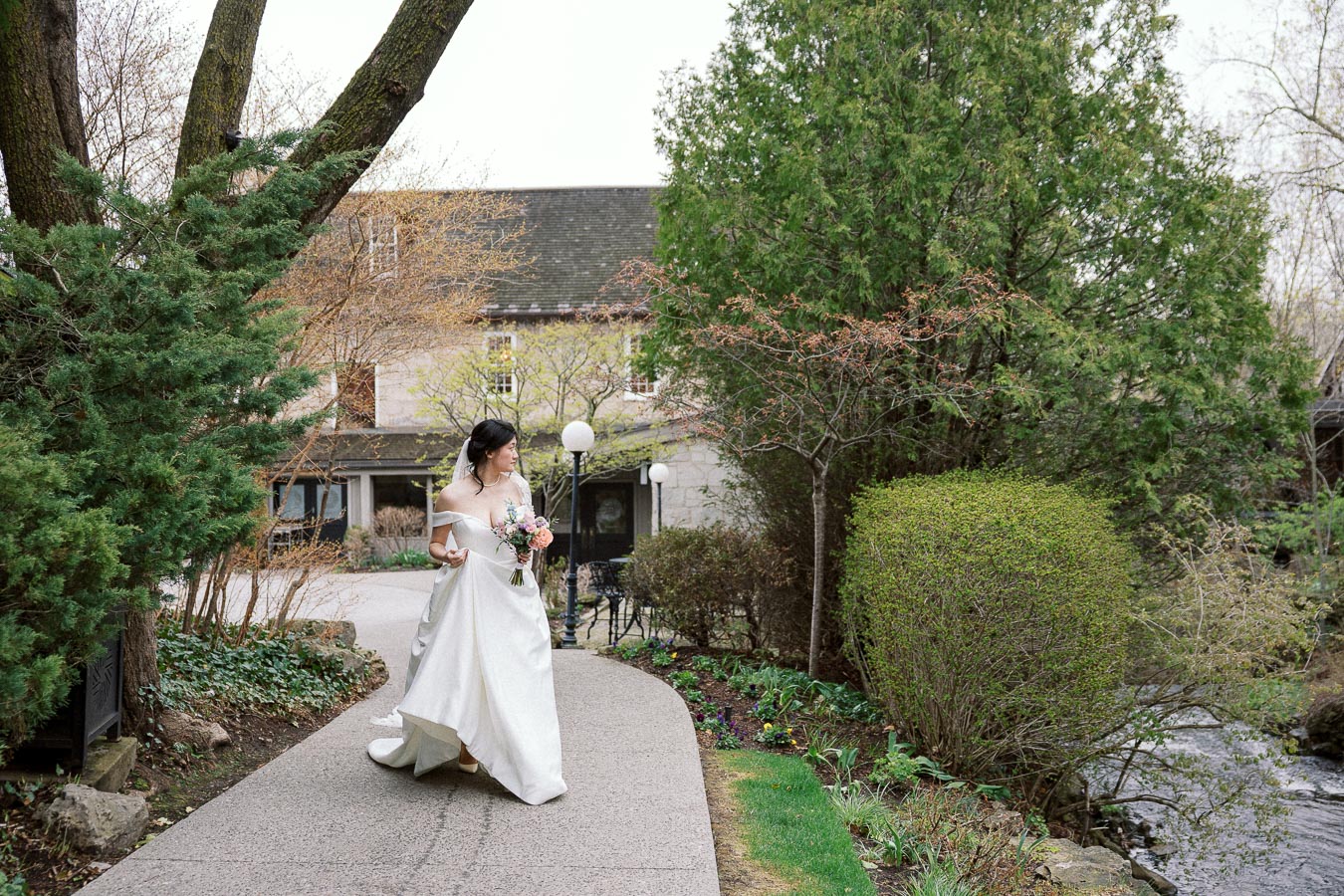 Bride in a white gown walking along a garden path with a bouquet