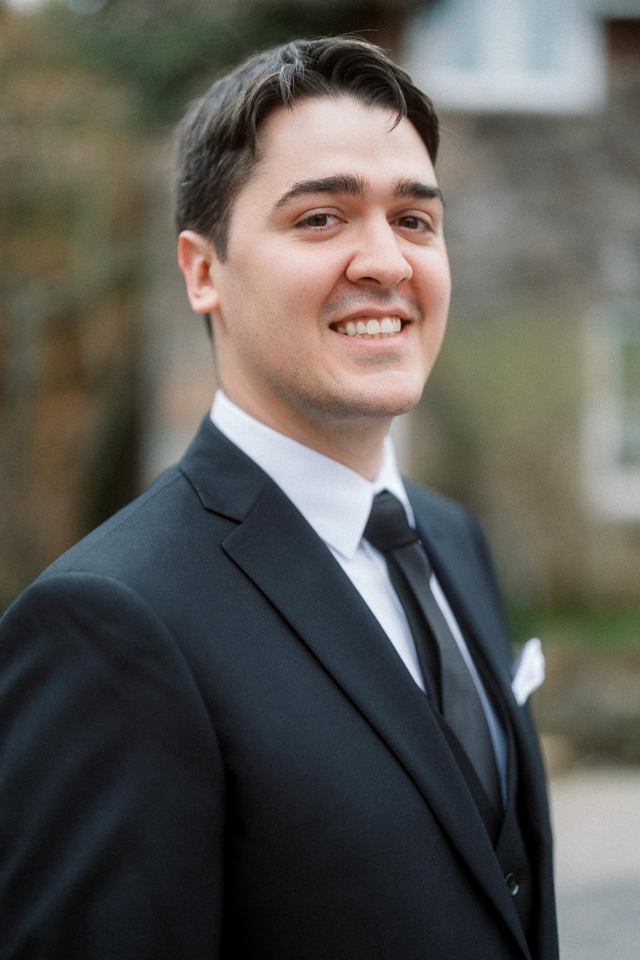 Smiling man in a black suit and tie outdoors during an engagement photoshoot