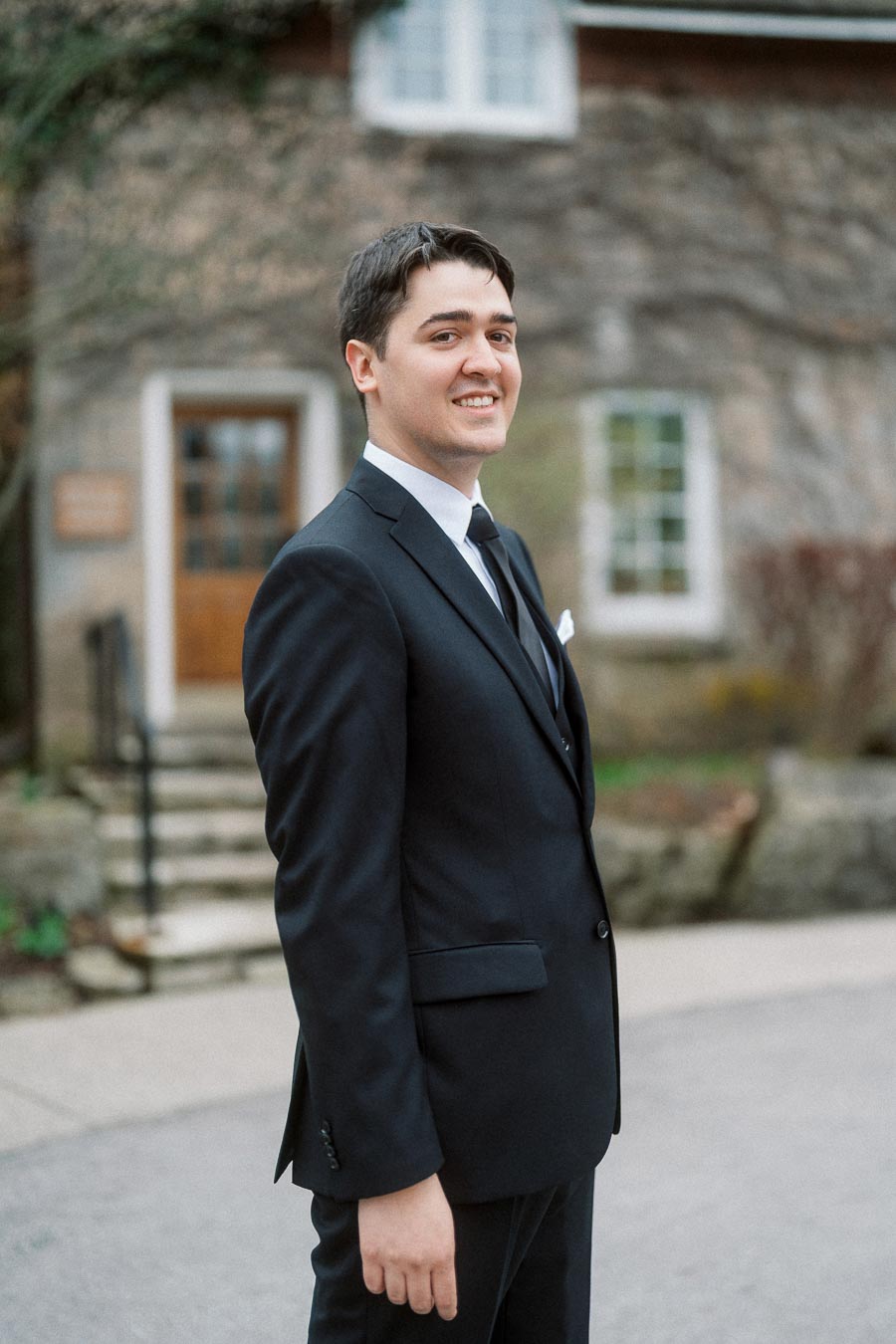 Man in a black suit smiling outside a stone building