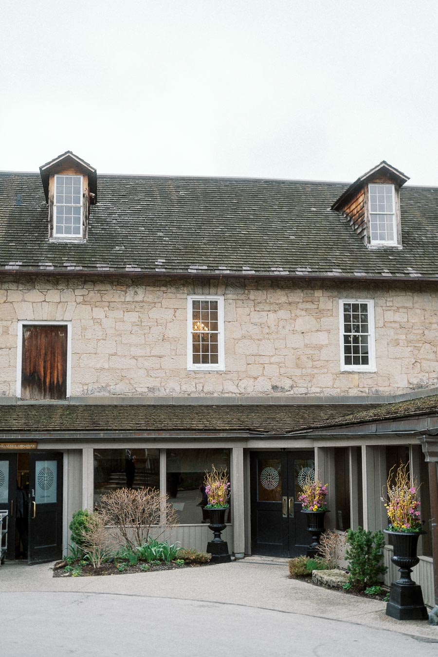 Stone building exterior with dormer windows, dark doors, and flower planters