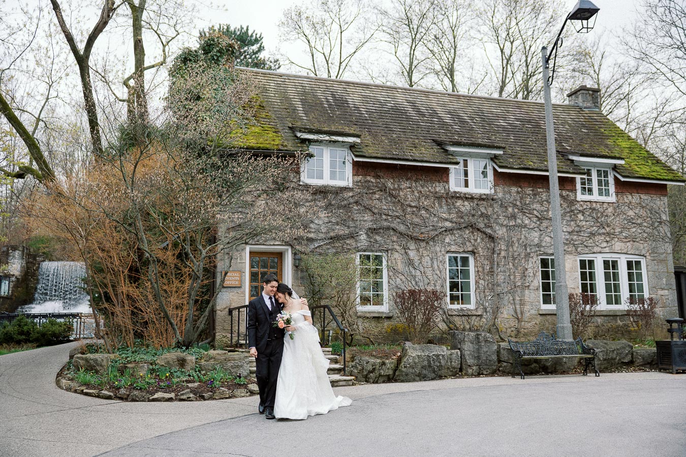 Couple in wedding attire standing together outside a rustic stone building.