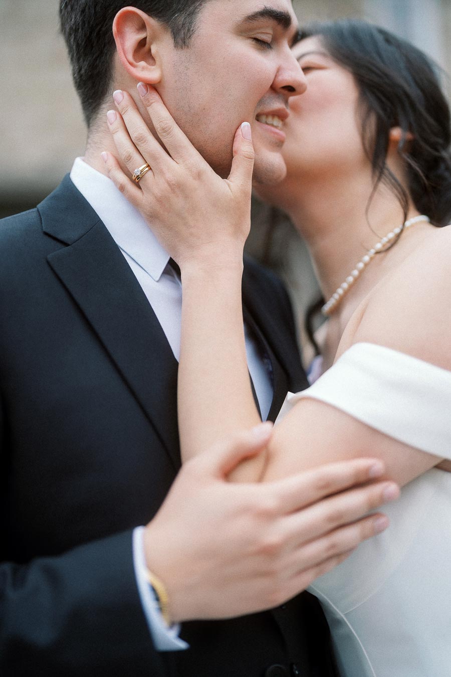 Close-up of an engaged couple embracing as she kisses his cheek, ring visible