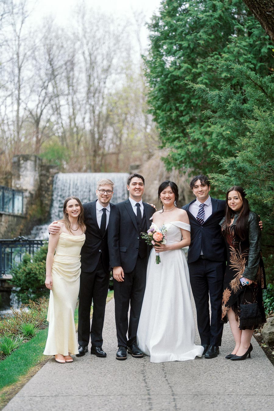 Wedding party posing together on a path beside a waterfall and evergreen trees