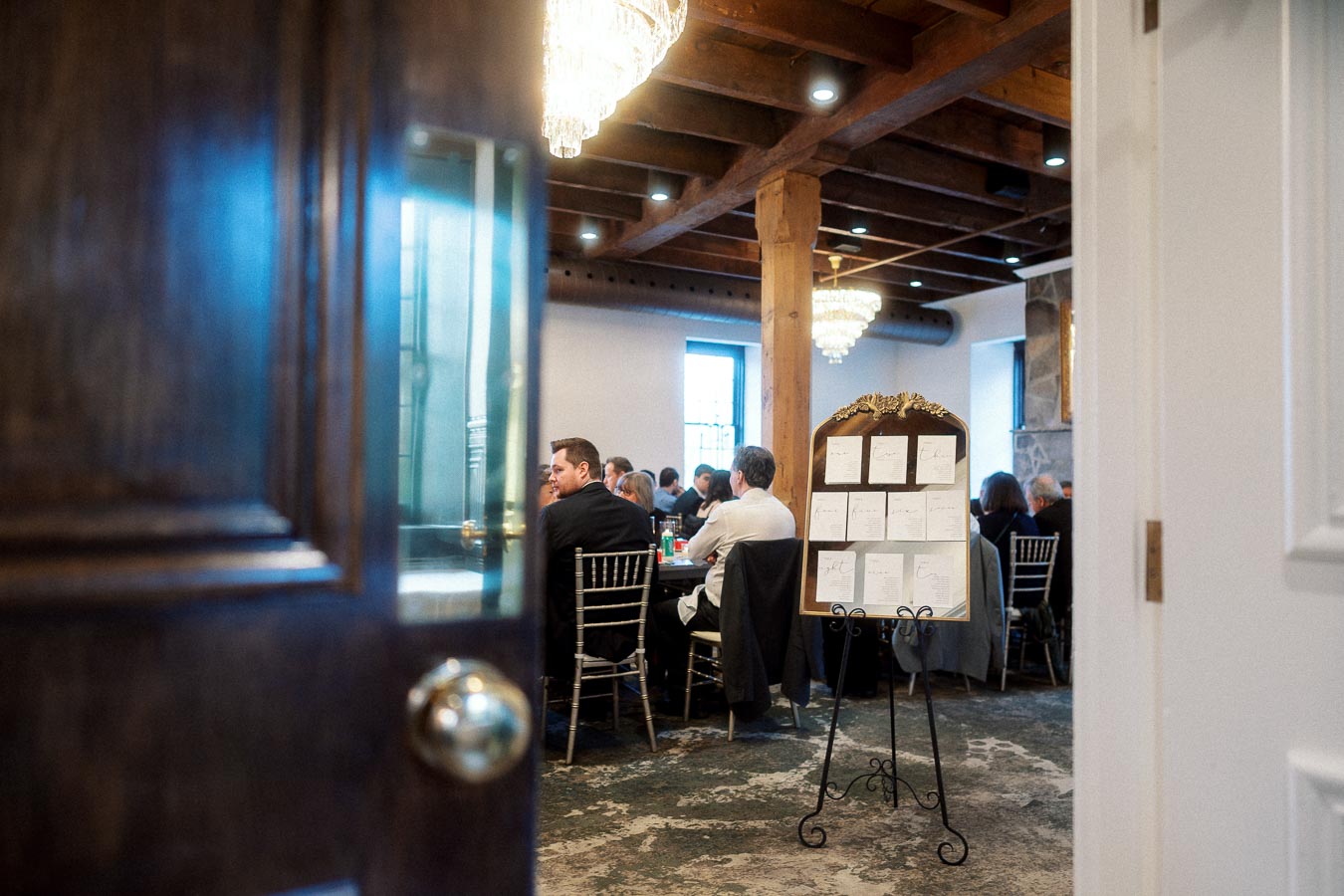 Open doorway looking into an indoor event with seated guests and a seating chart.